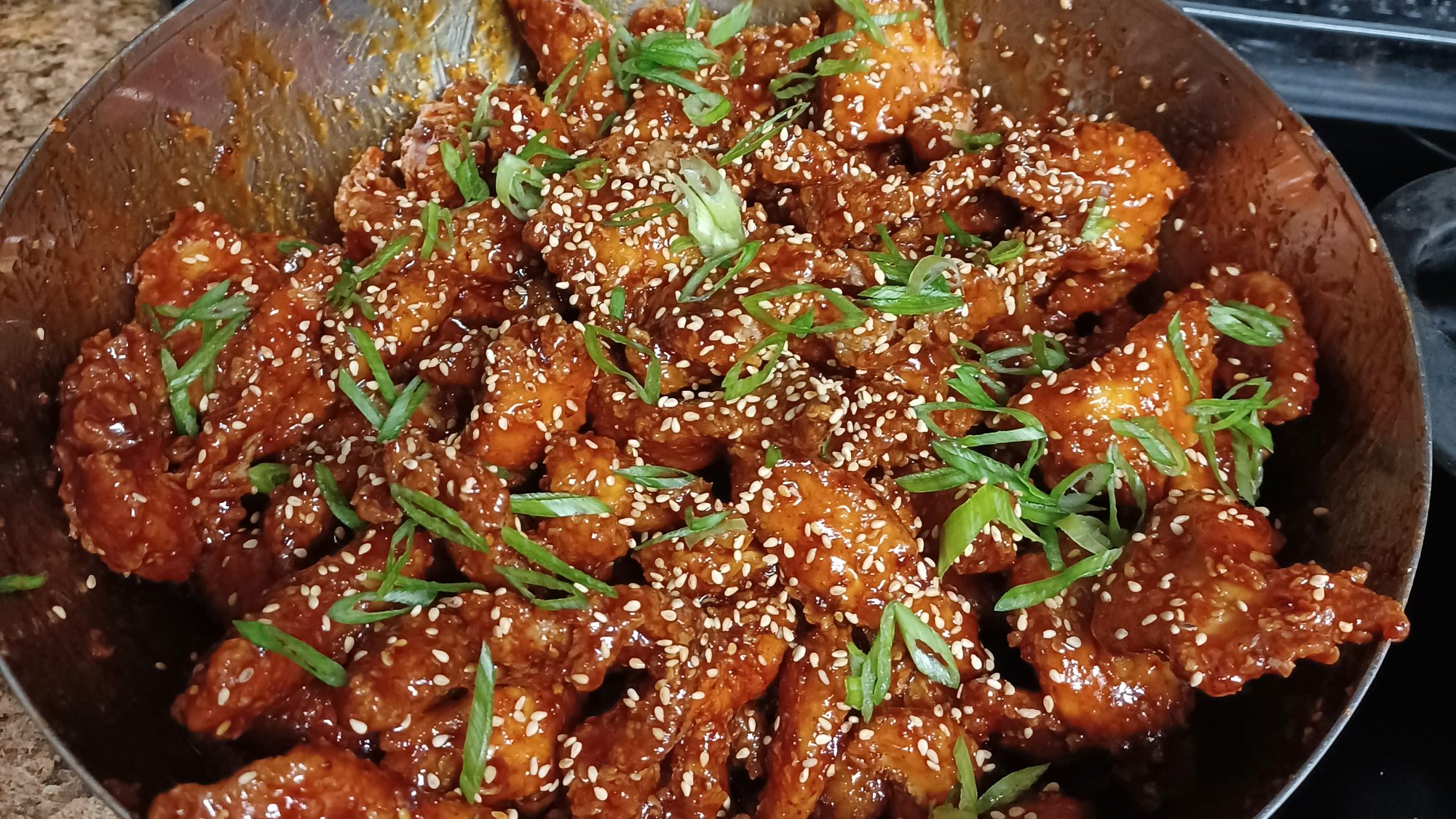 A pan of sticky glazed wings topped with sesame seeds and green onion
